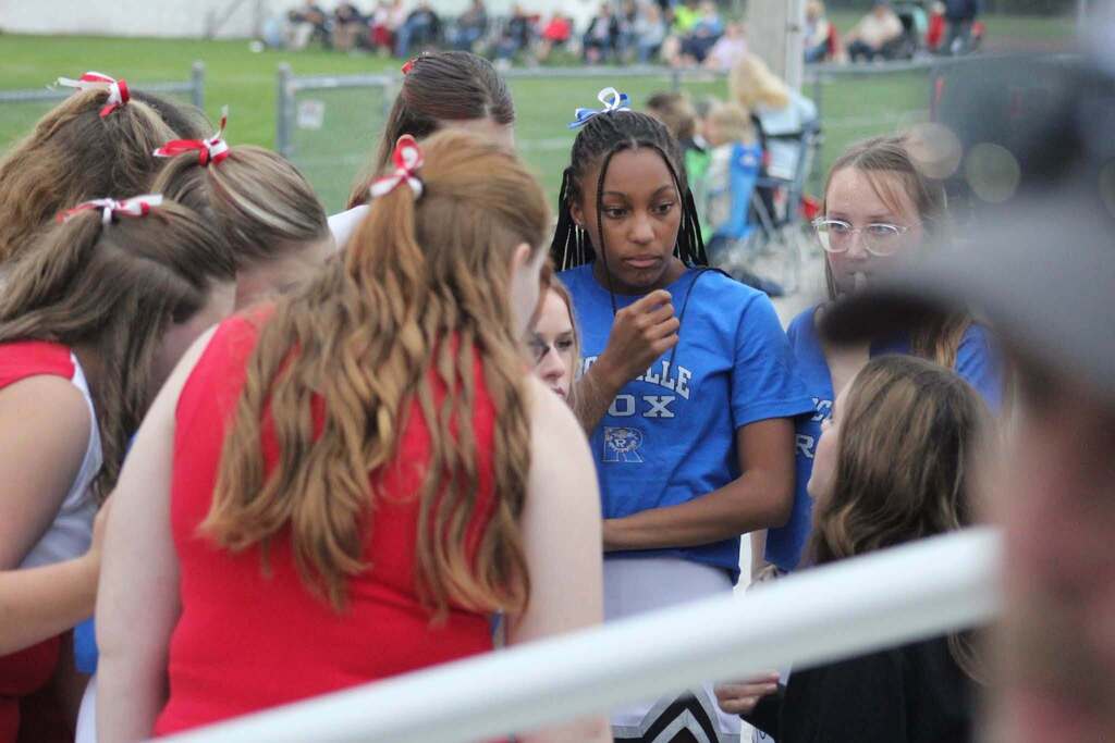 Cheerleader in ROX and Warrior uniforms huddled together listening to their cheer coach. 