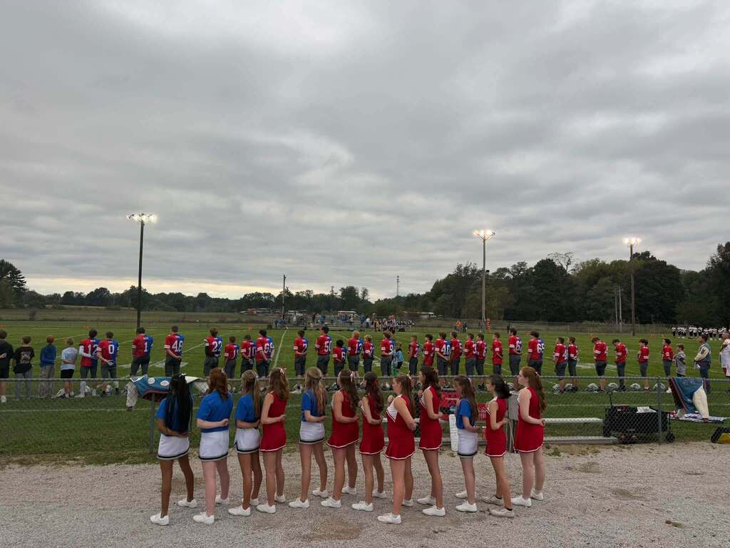 PHMS Cheerleaders and Football Players lined up in their ROX and Warrior uniforms with their hands on their hearts for the national anthem.