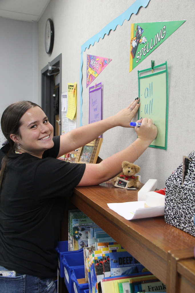 Education Professions student writing on the paper sleeve hanging on the wall while looking at the camera smiling.