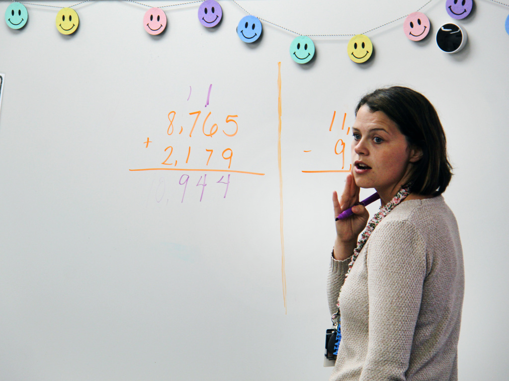 The teacher with a dry erase marker in her hand, after writing on the dry erase board, listening to her students question. 