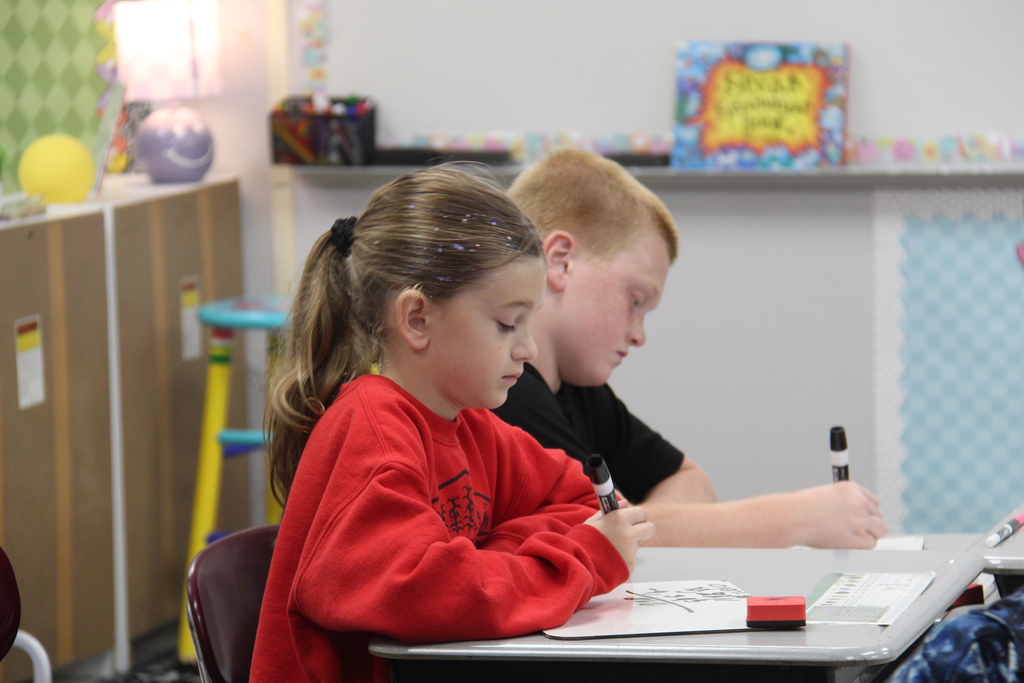 A girl and a boy working on their white boards, trying to figure out a math problem.