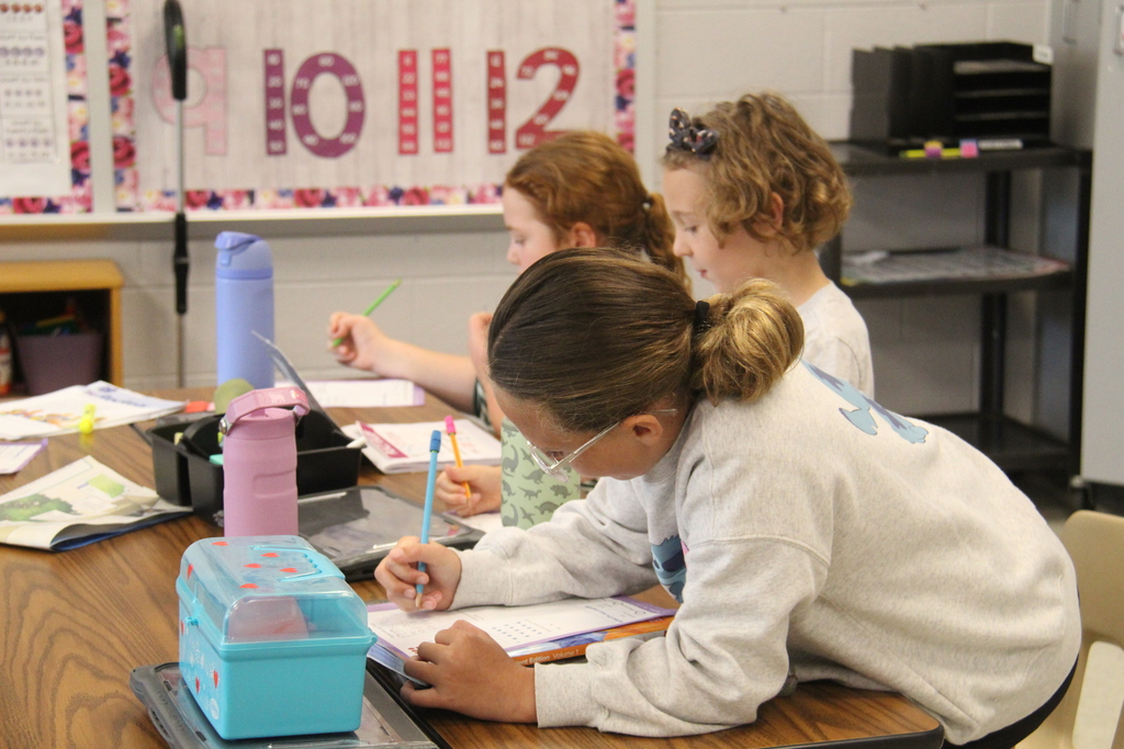 3 girls sitting together, working on their worksheets.