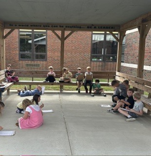 1st grade students all sitting around under the pavilion working on their math worksheets. 