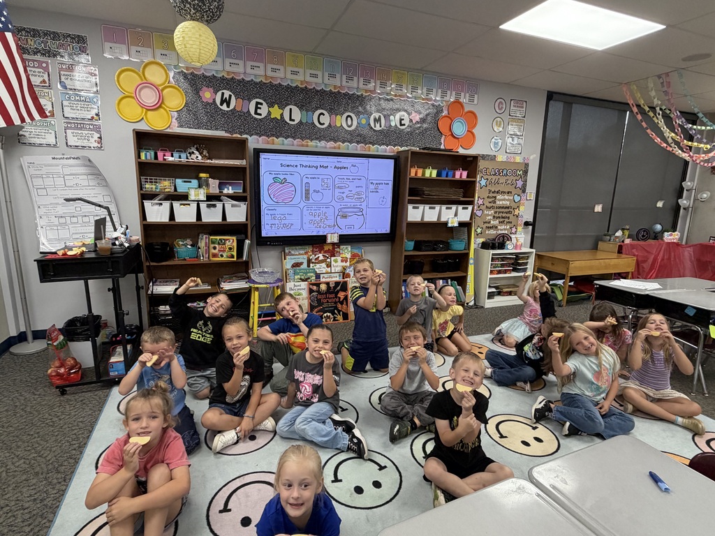 Students sitting on the floor facing the camera, showing off their apple smiles. 