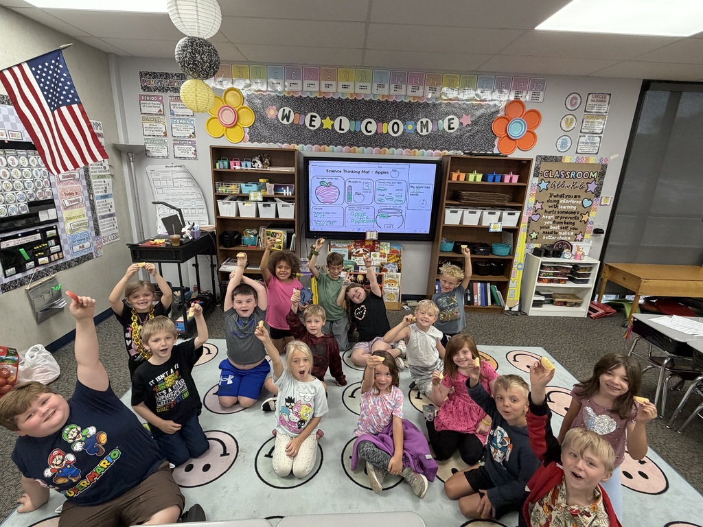 Students sitting on the floor, facing the camera, showing off their apple smiles.