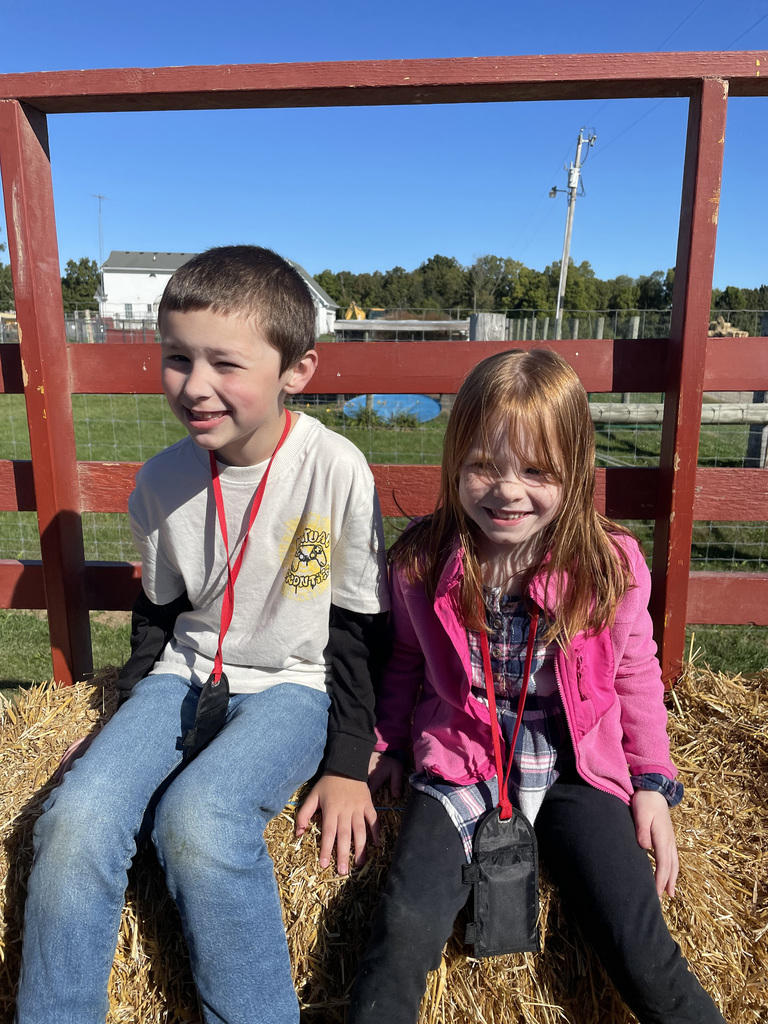 2 students smile for a photo while sitting on the hay trailer, waiting for a hay ride!