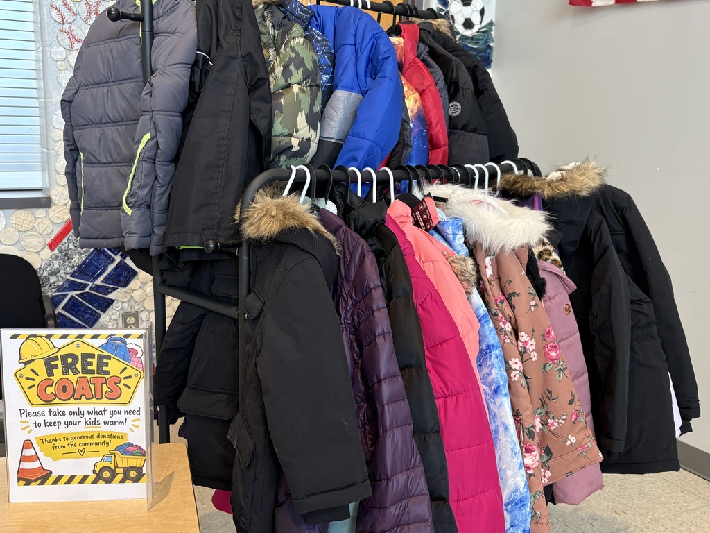 Photo of winter coats on a rack with a signs that says Free Coats. Please take only what you need to keep your kids warm! Thanks to the generous donations from the community!