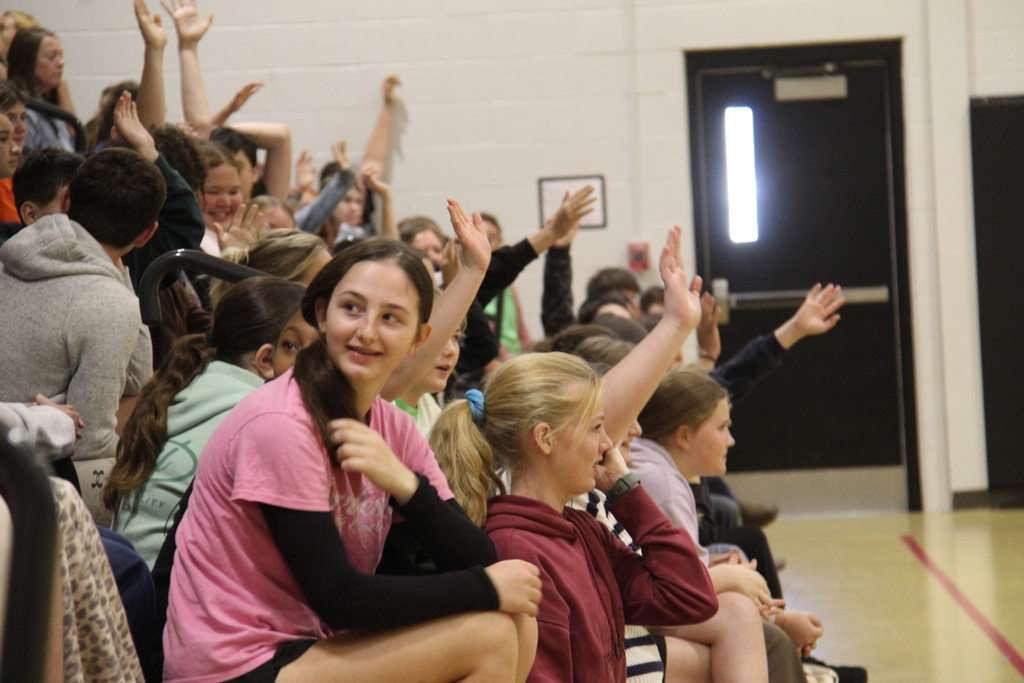 Students in the audience raising their hands to volunteer to help.