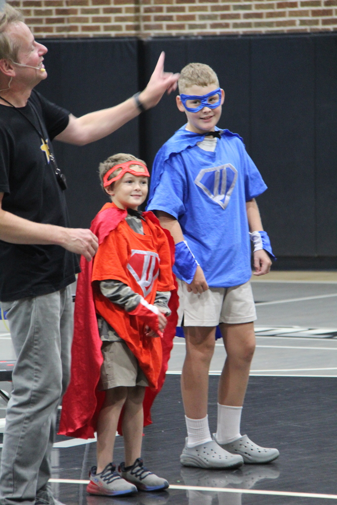 Students standing with their super hero costumes on after competition to see who can suit up fastest and the speaker. 