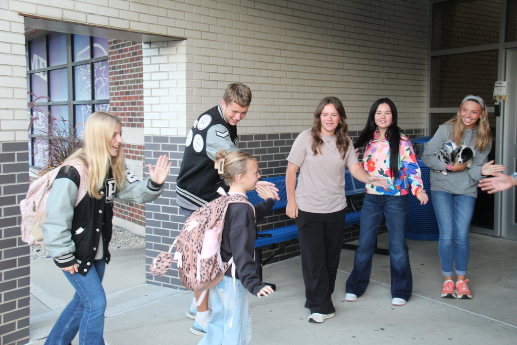 Members of the Tennis, Cross Country, and Golf teams line up along the sidewalk to five high fives to one of the students as she walks into school. 