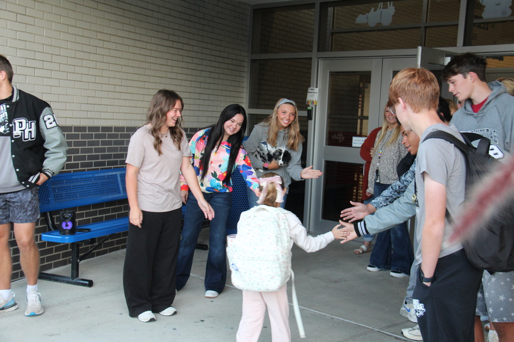 Members of the Tennis, Cross Country, and Golf teams line up along the sidewalk to five high fives to one of the students as she walks into school. 