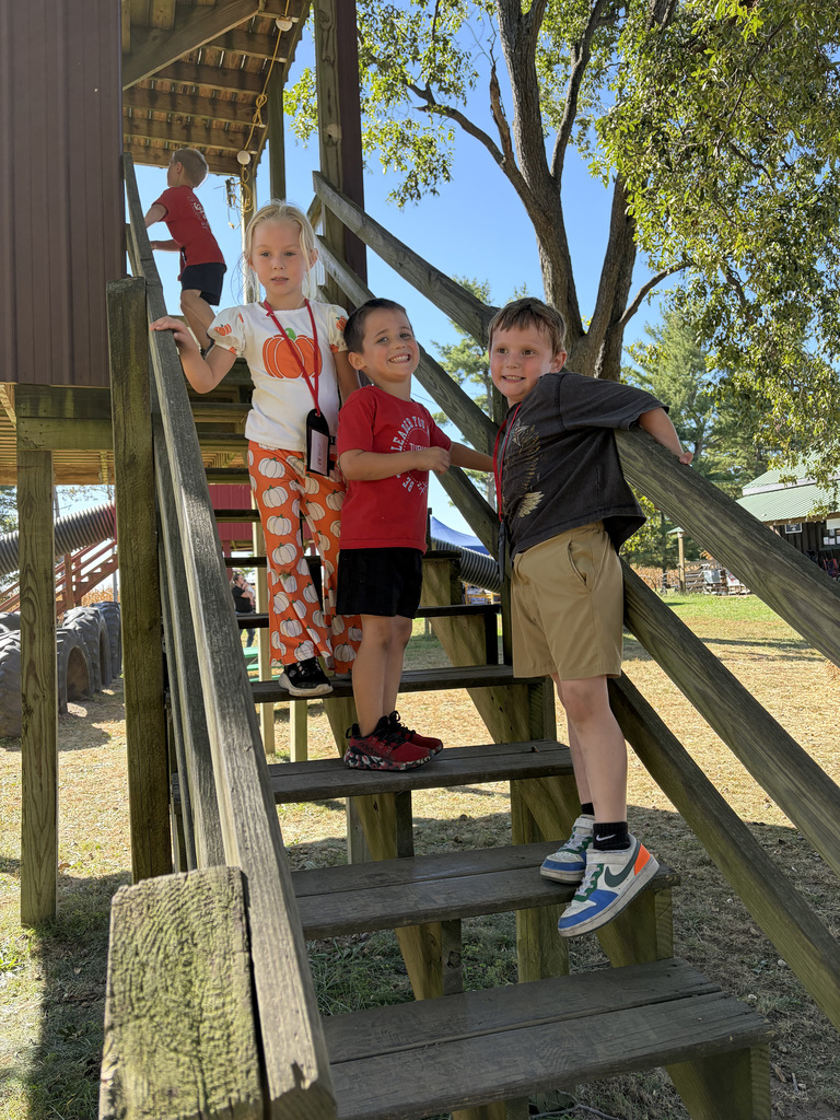 3 students pose for a photo on the stairs that go up to the large tunnel slide. 