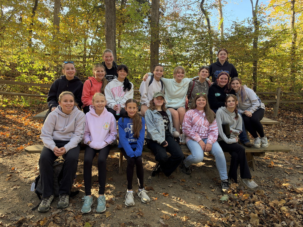 A group of students sit on a picnic table, posing for a photo. 
