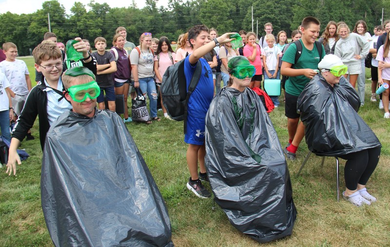 three people wearing trash bags and goggles getting slimed by students