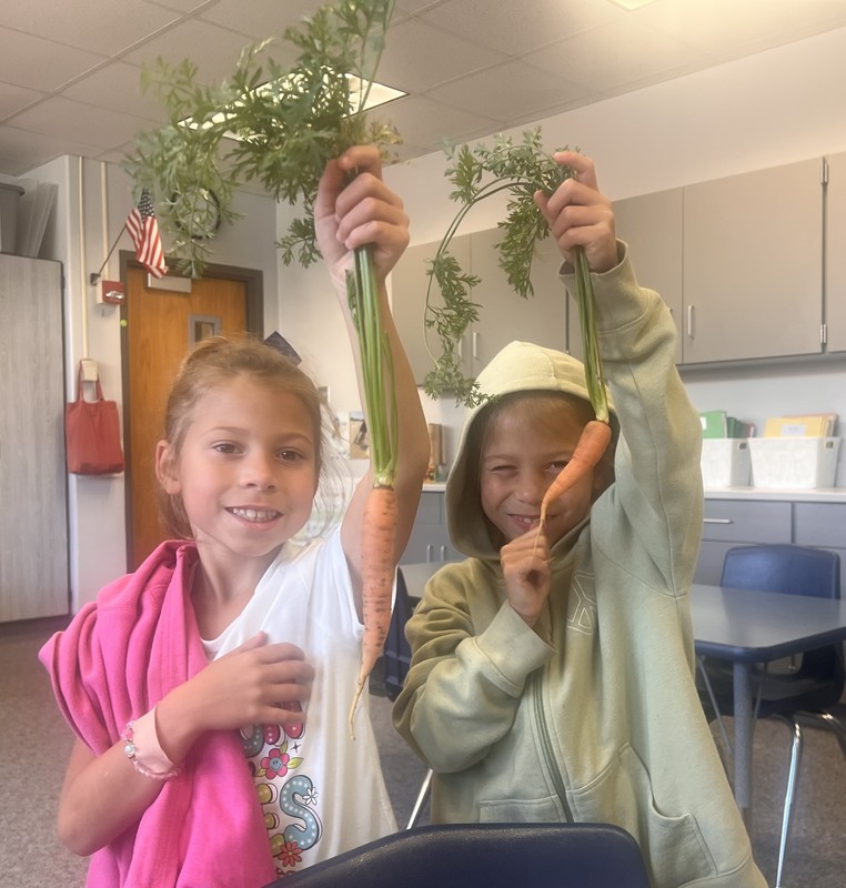 two students holding up carrots