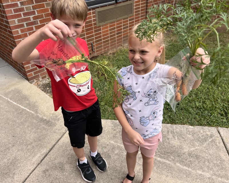 two students holding up carrots