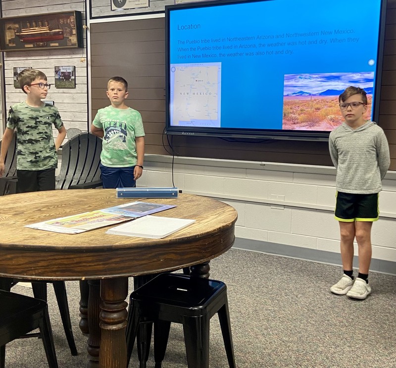 three students standing by a computer monitor talking about Native Americans