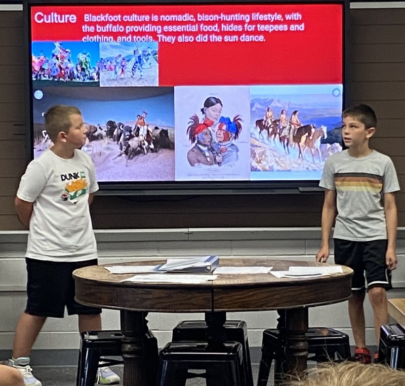 two students standing by a computer monitor talking about Native Americans