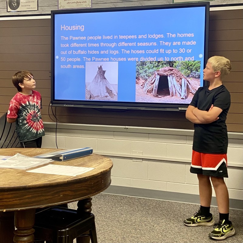 two students standing by a computer monitor talking about Native Americans
