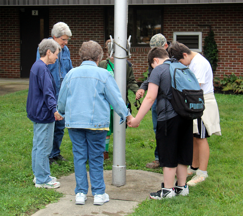group of students and adults standing around the flagpole for a time of reflection