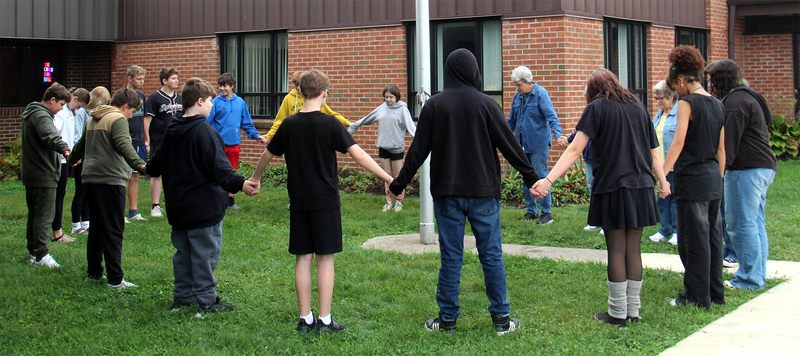 group of students and adults standing around the flagpole holding hands for a time of reflection