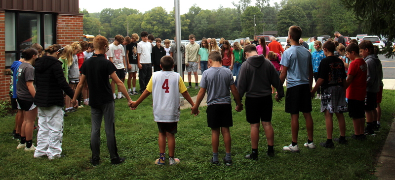 group of students standing around the flagpole for a time of reflection