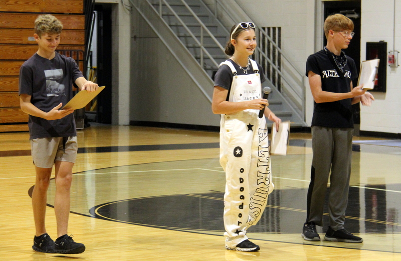 three students standing in the gym talking to other students
