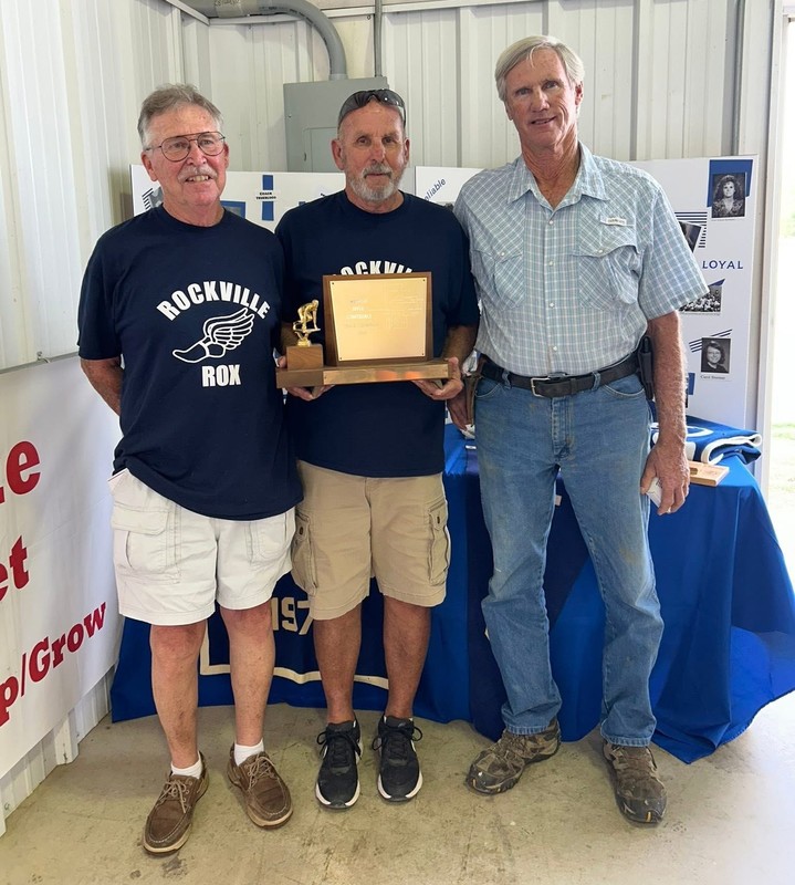 three men standing together with one holding a trophy