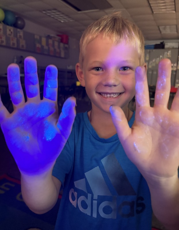 a boy holding up his hands with one of them having Germ Glo on it