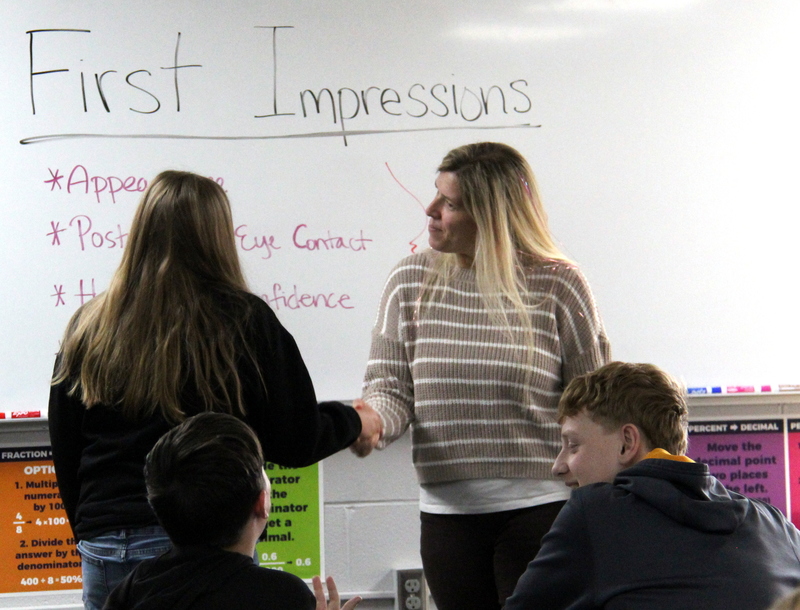 teacher and a student shaking hands while two students watch