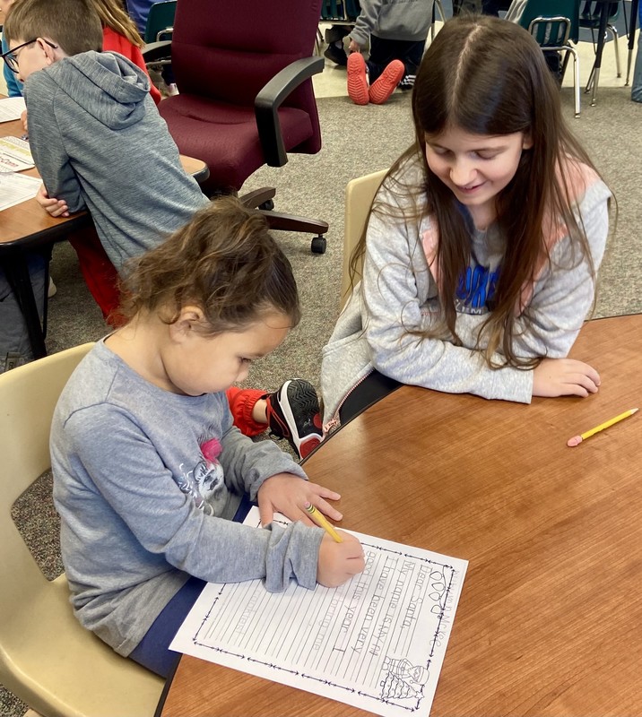 two girls sitting at a table and writing a letter to Santa