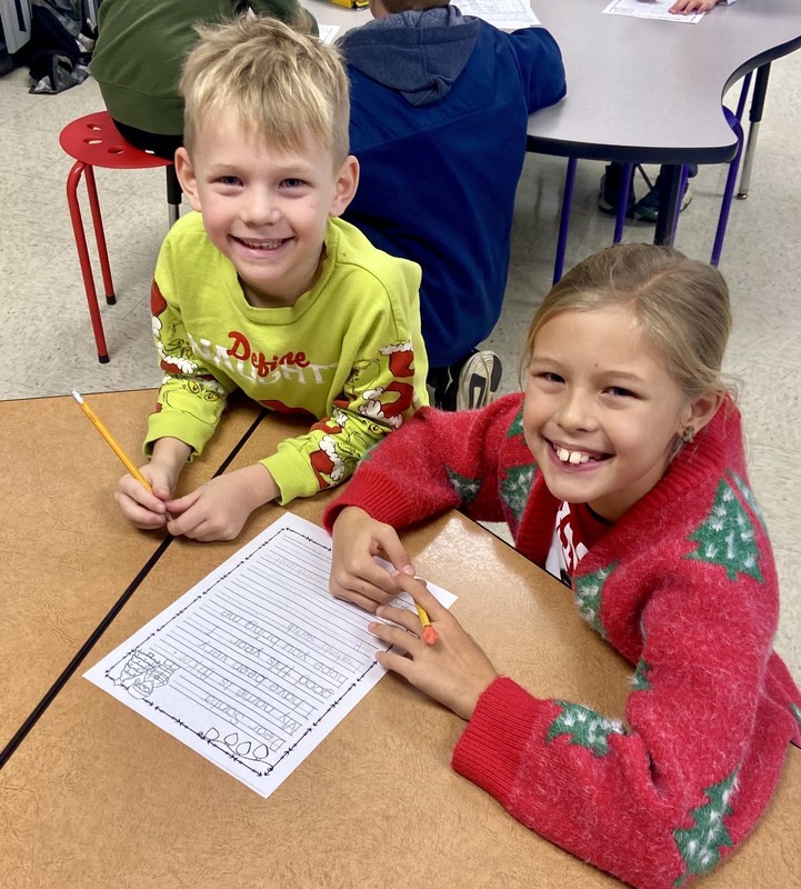 a boy and a girl sitting at a table and writing a letter to Santa