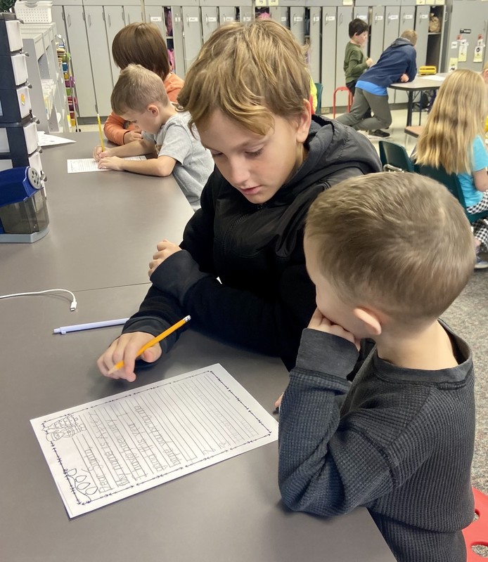 two boys sitting at a table and writing a letter to Santa