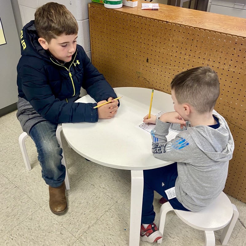 two boys sitting at a table and writing a letter to Santa