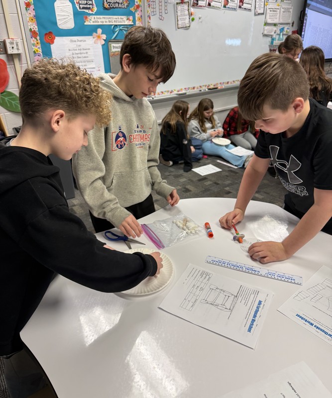 three boys working on an earthquake design using marshmallows and toothpicks