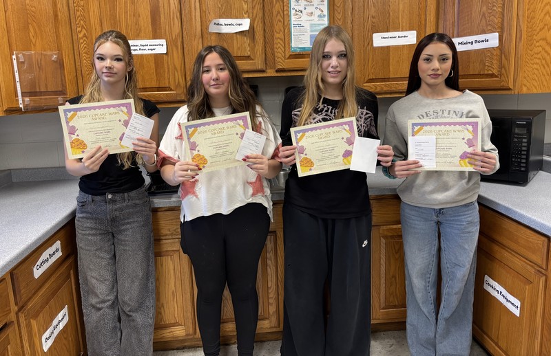 four students standing in a classroom kitchen holding certificates