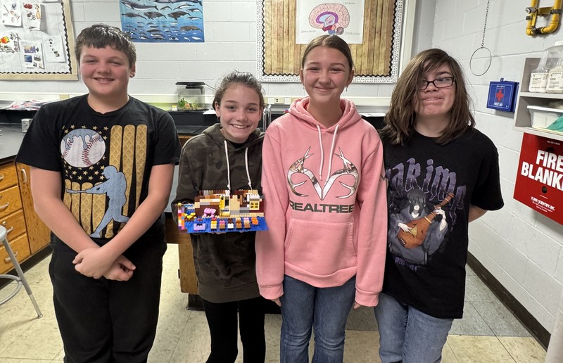 four students standing in a line with one of them holding a theater set made out of Legos