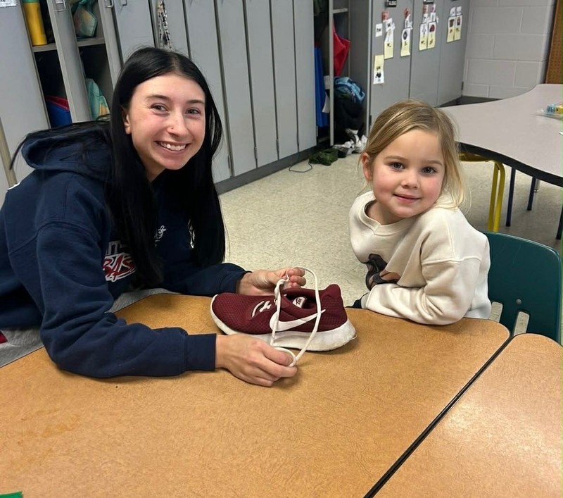 a high school student helping a kindergarten student learn to tie their shoe