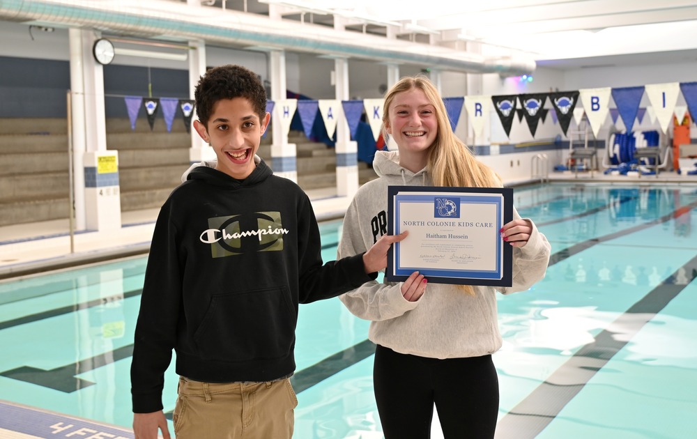 Two students pose with a Kids Care certificate in front of the pool.