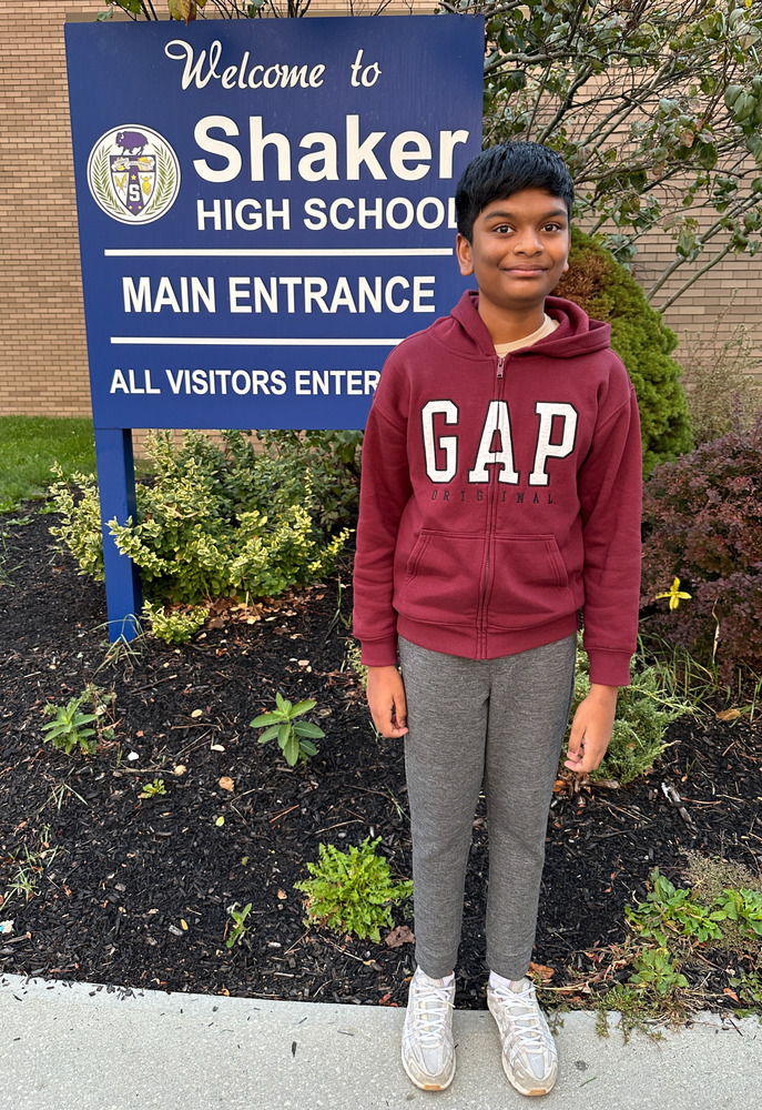An image of a student standing in front of the Shaker High School main entrance sign.
