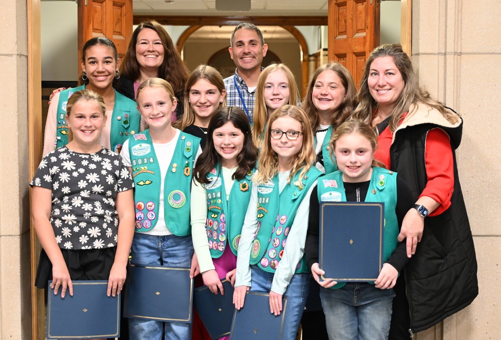 An image of nine Girl Scouts posing with certificates received for being named October Kids Care recipients.