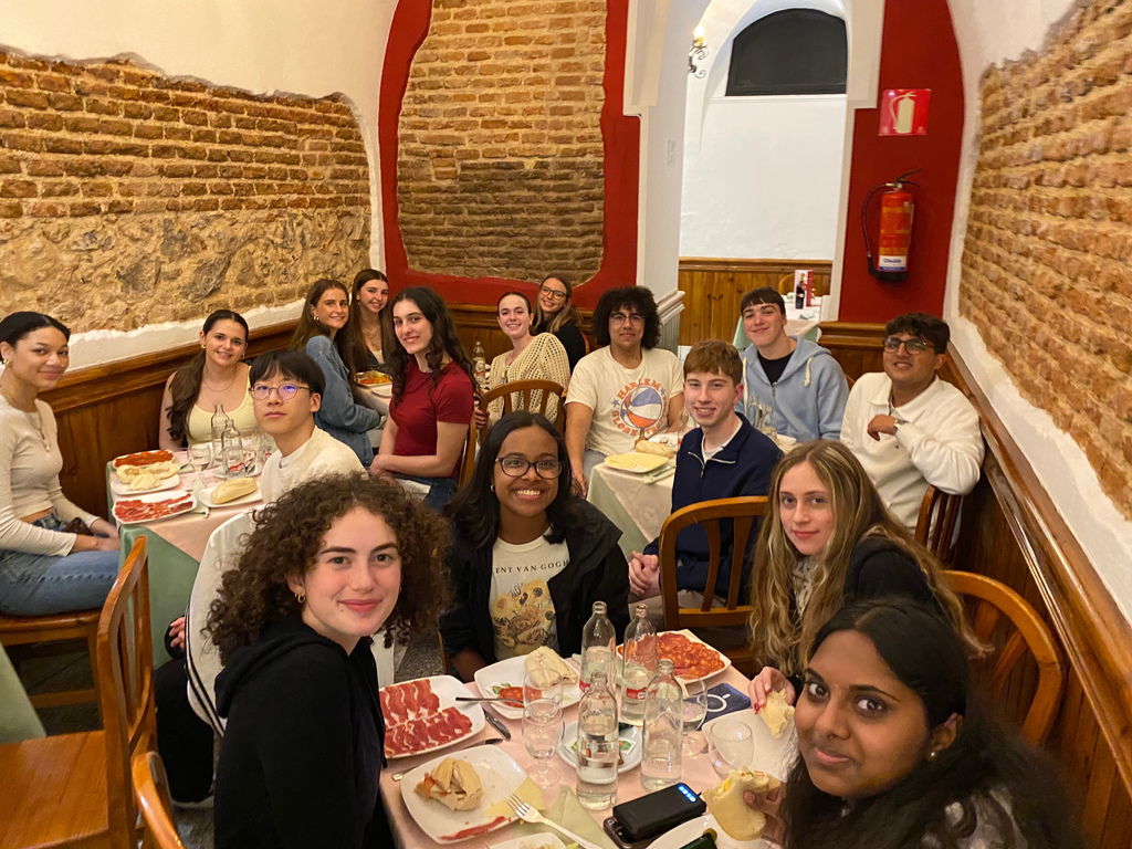 An image of a group of students sitting at tables while they eat dinner together.