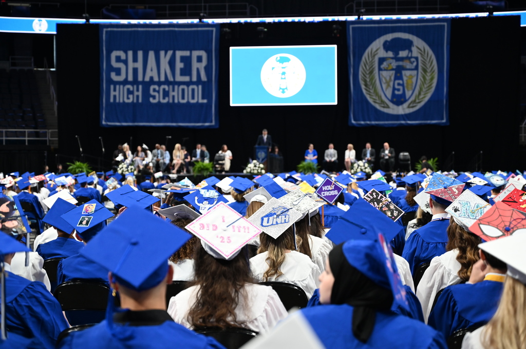 An image of hundreds of graduates in the foreground facing the graduation stage in the arena.