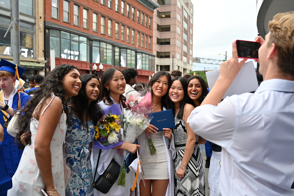 A student takes a photo on his phone of six graduates posing together.