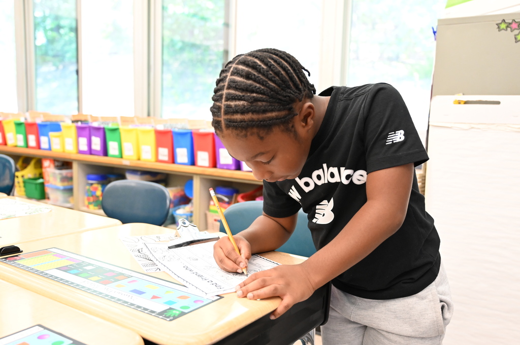 A student writes with a pencil on his paper at a desk.