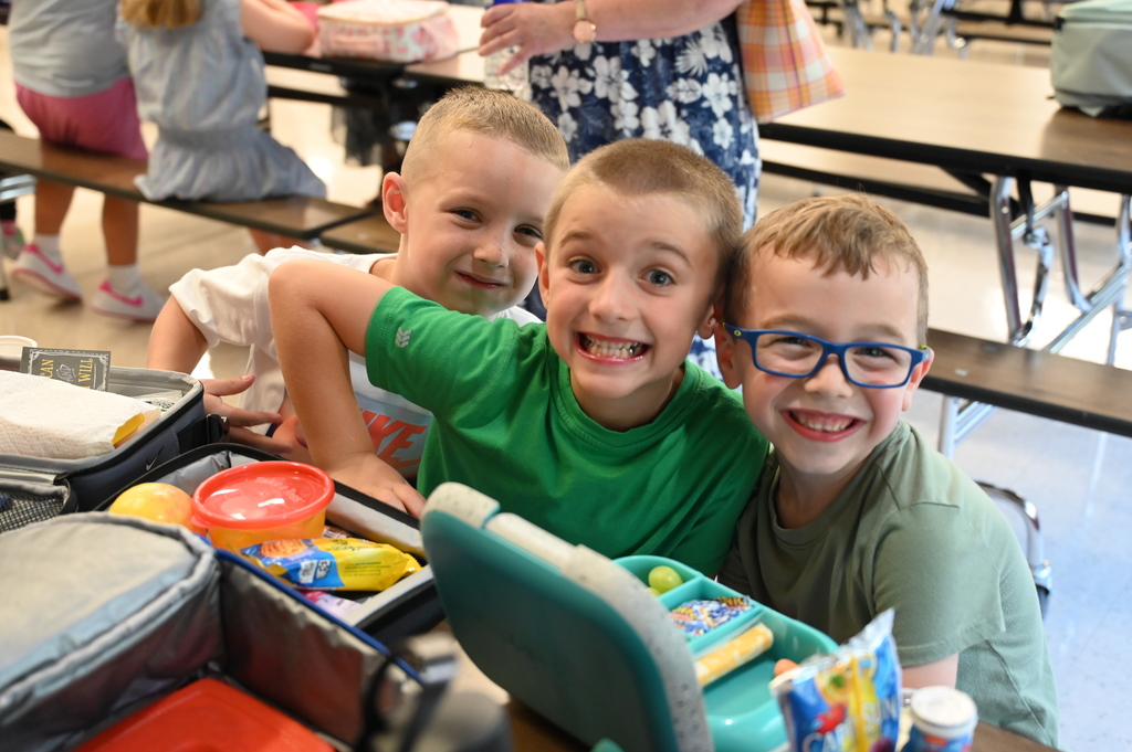 Three students smile while sitting at the lunch table in the cafeteria.