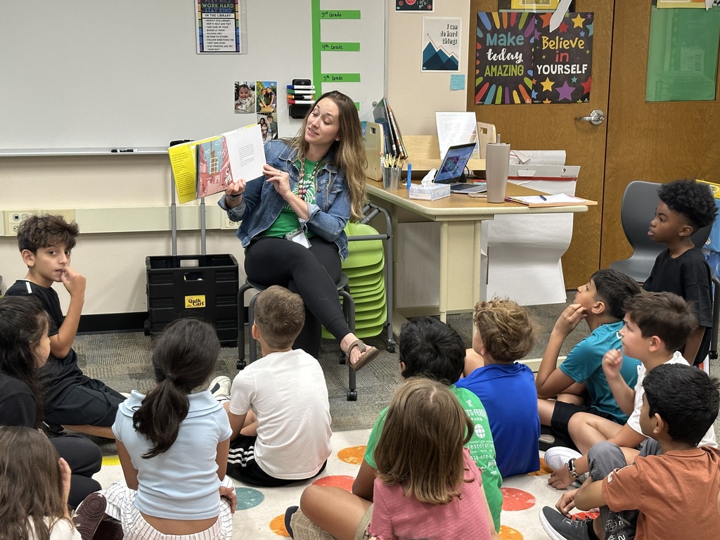 Students look on from the carpet as the librarian reads them a book.