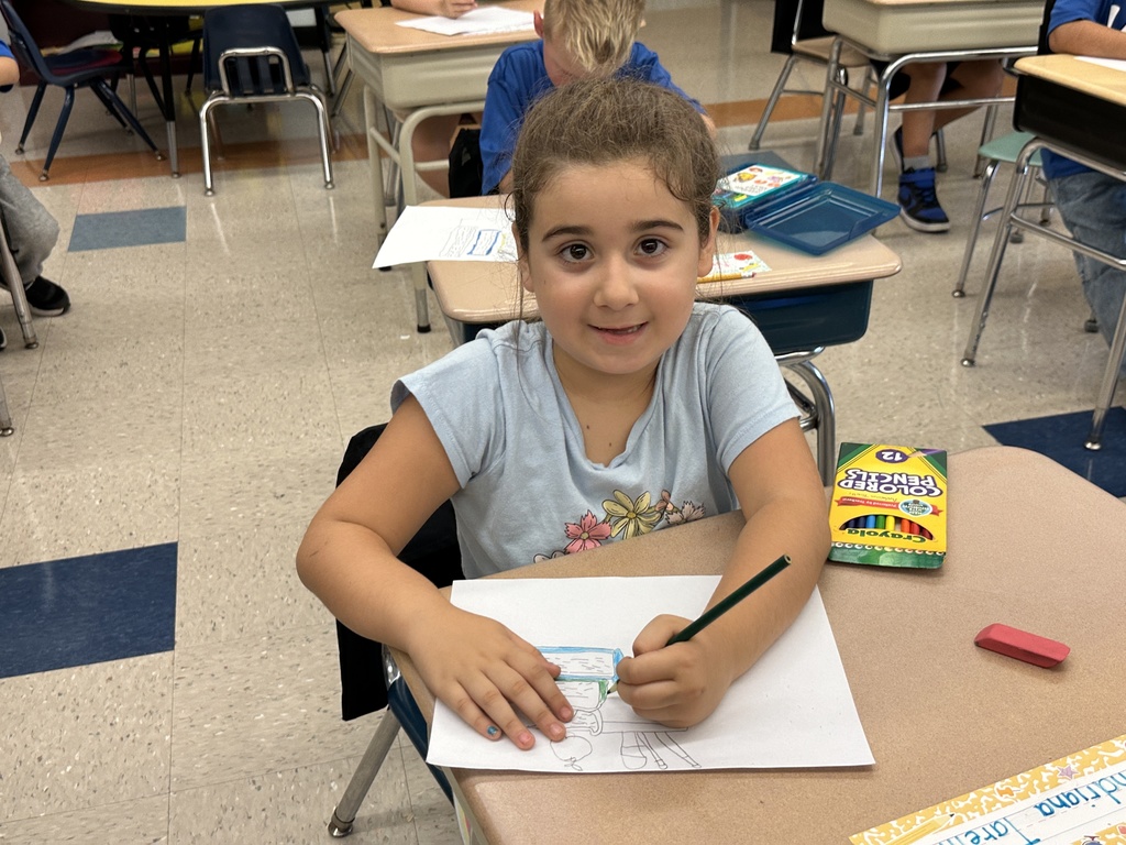 A student smiles as she colors at her desk.