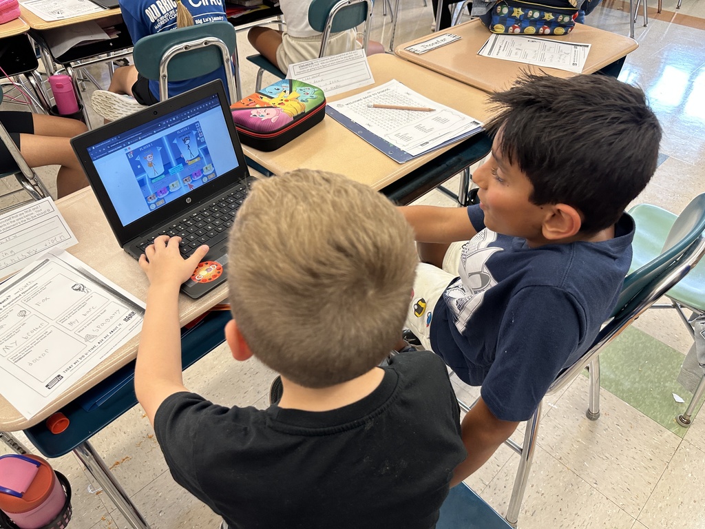 Two students sit together and work at a Chromebook.