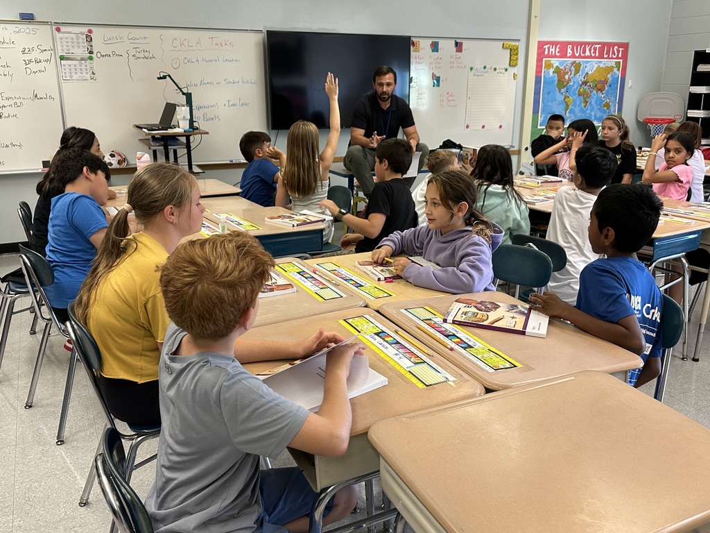 A teacher sits at the front of the room and calls on students to answer questions.
